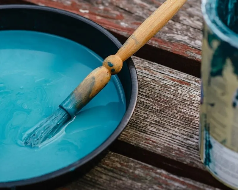 Paintbrush dipped in blue paint, ready for use on a wooden surface, ideal for beehive painting